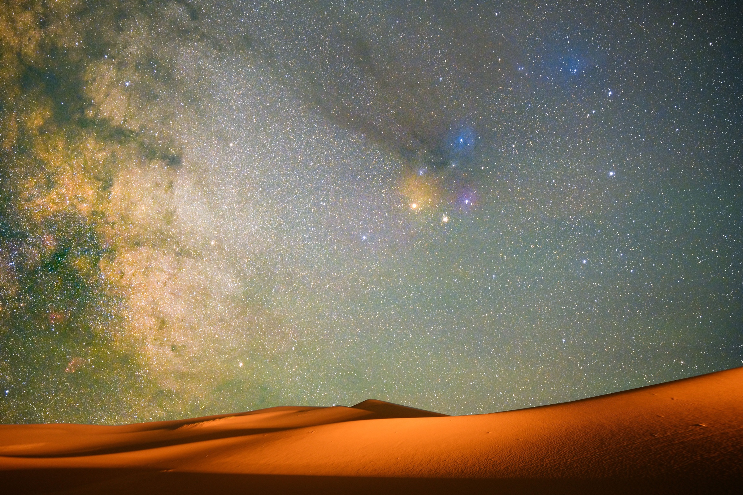 A star-filled sky above glowing desert dunes